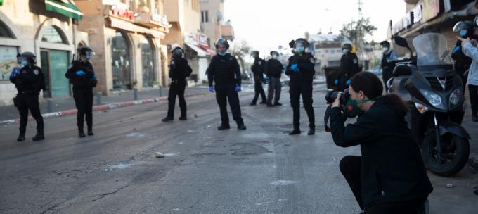A photo journalist kneels to capture an image surrounded by police