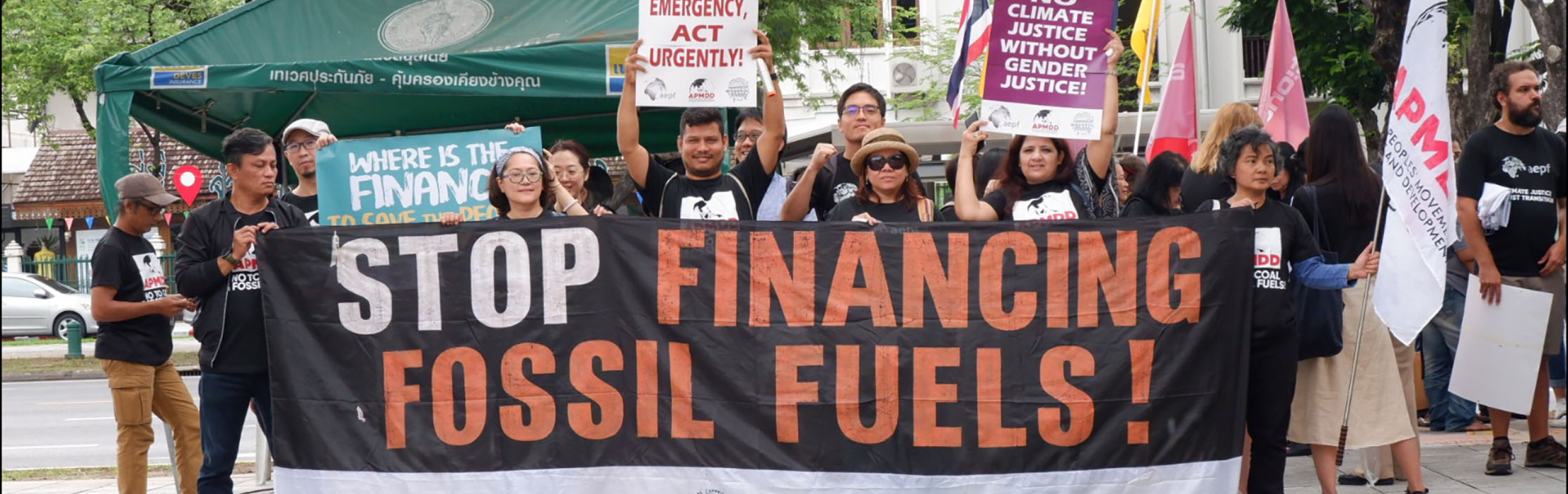 Donzens of people gathered behind a sign that reads Stop Financing Fossil Fuels
