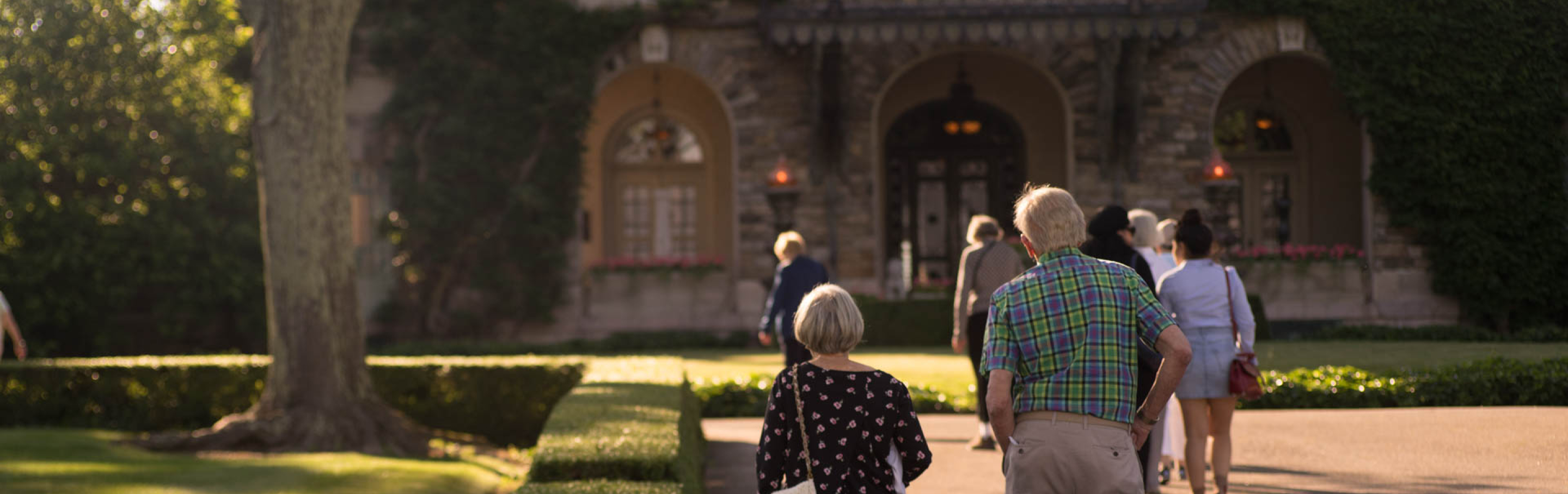 several people walk along an outdoor path in with Kykuit, the historic Rockefeller estate at Pocantico, in the background