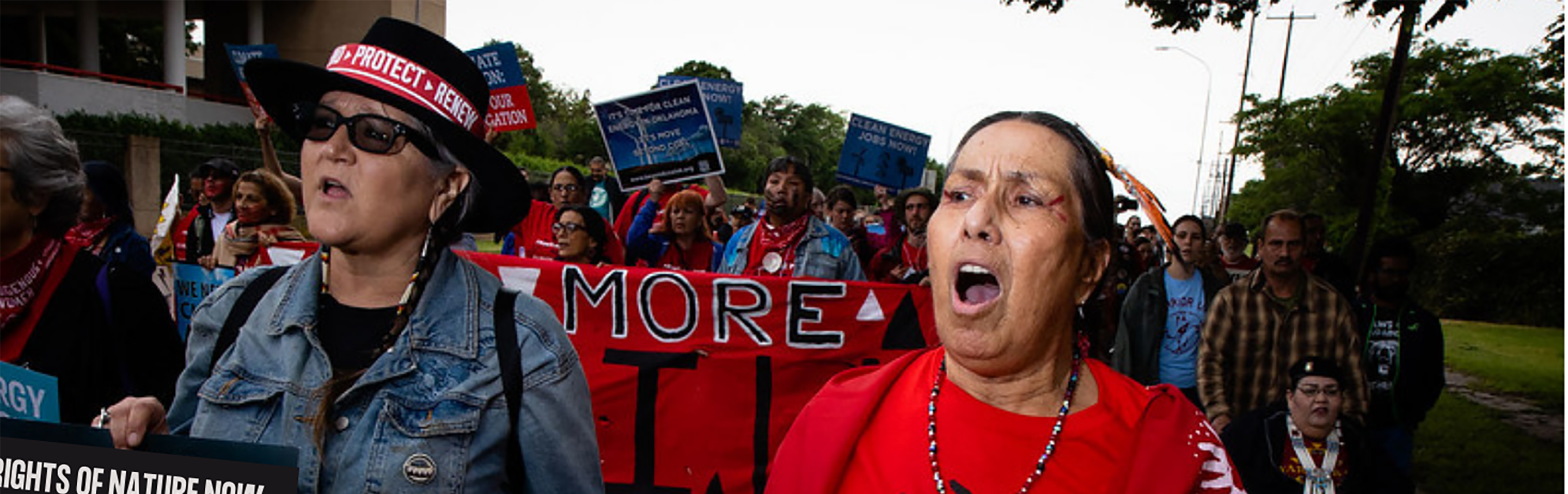 An indigenous women marches with a sign that says e are here to protect earth
