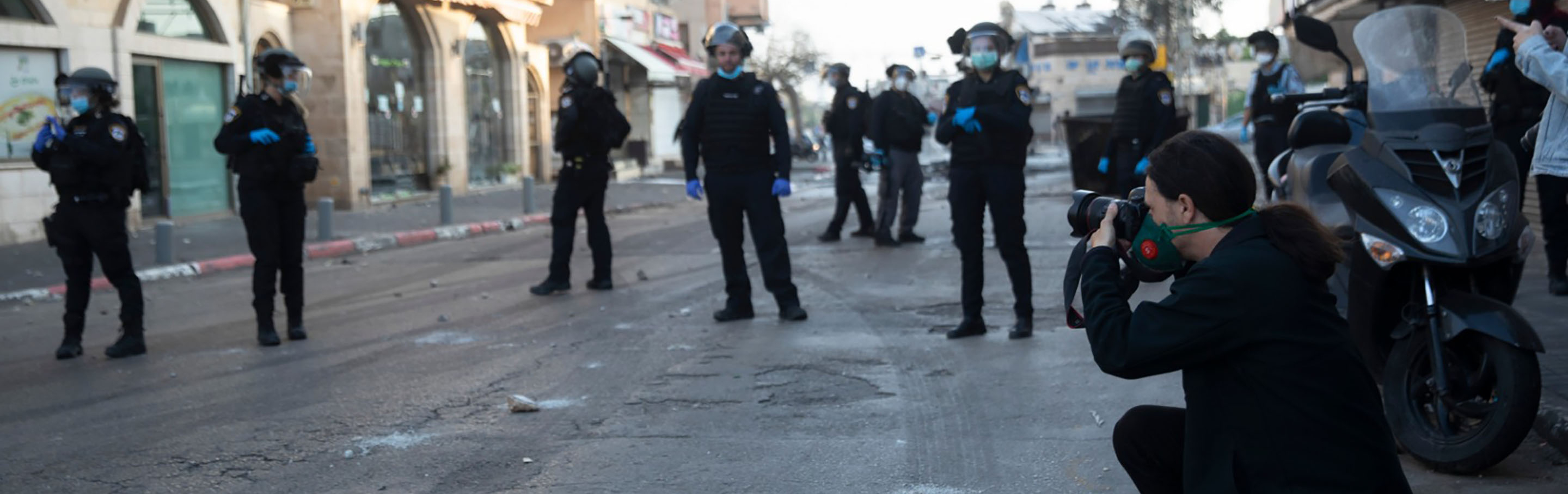 A photo journalist kneels to capture an image surrounded by police