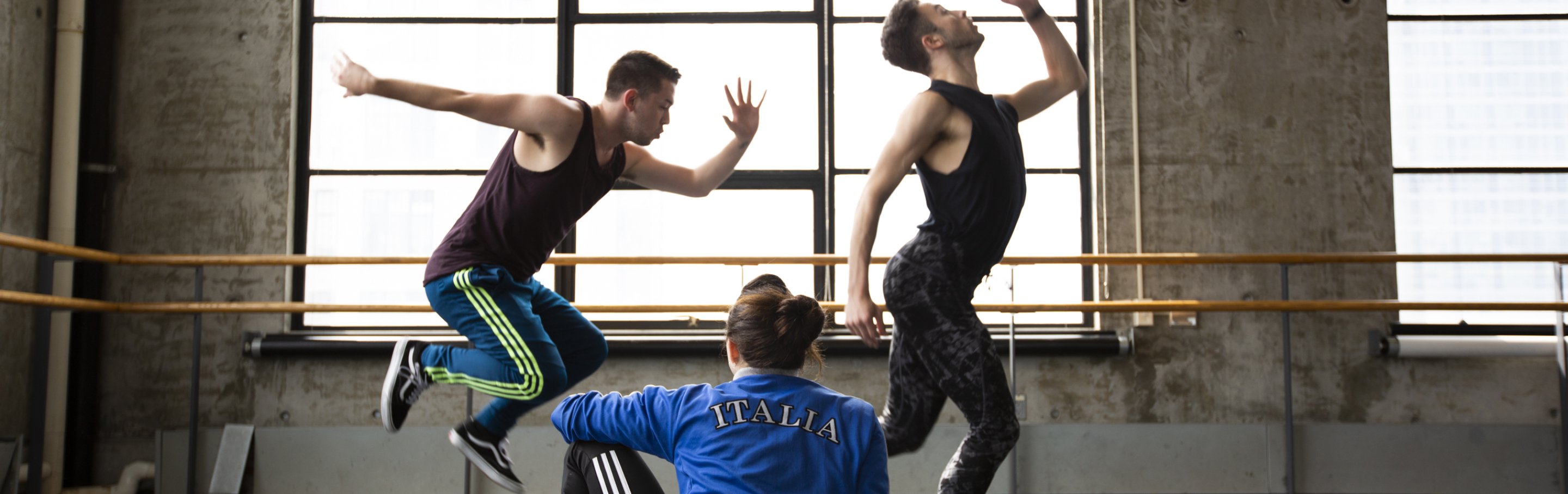 Three dancers practice in a warehouse.