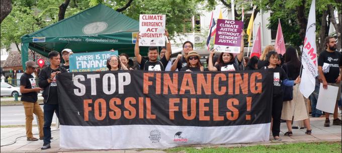 Donzens of people gathered behind a sign that reads Stop Financing Fossil Fuels