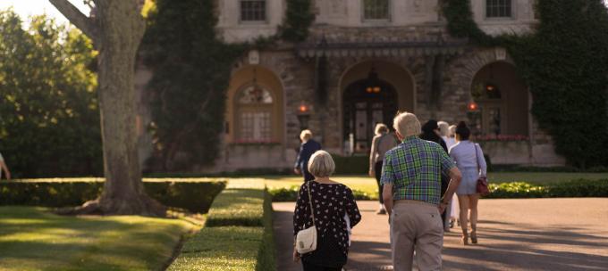 several people walk along an outdoor path in with Kykuit, the historic Rockefeller estate at Pocantico, in the background