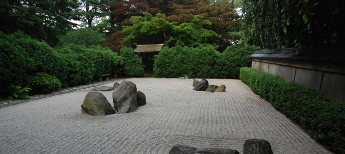 Rocks placed among patterned white gravel surrounded by green shrubbery