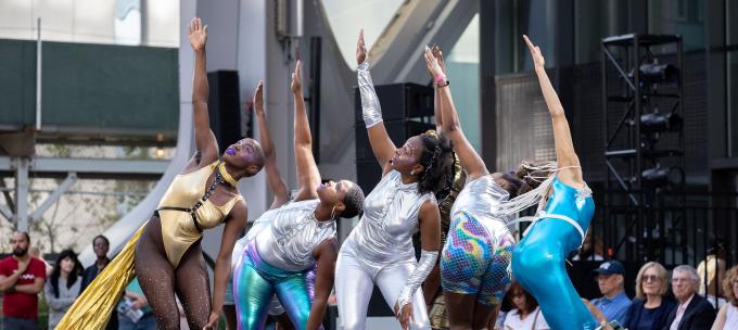 Fours black female dancers in shiny spandex put on a show for an outdoor audience.