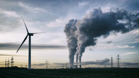 A wind turbine in front of a smoke stack