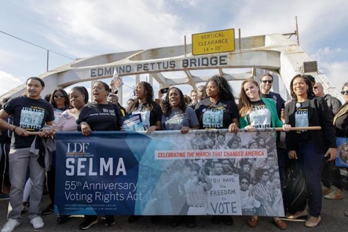 protesters demonstrate on the Edmund Pettus bridge in Selma, AL with signs commemorating the voting rights act.