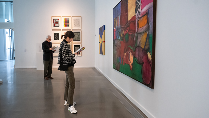 visitors examine colorful painting hung in the gallery