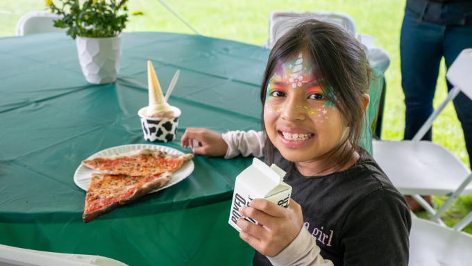 Child smiles while eating pizza and drinking water