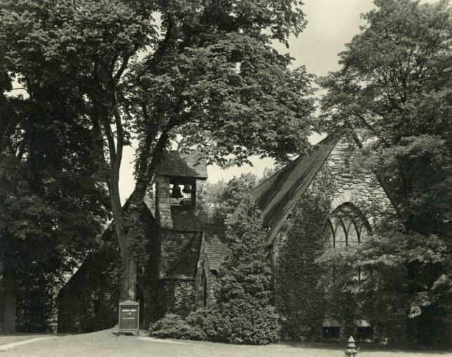 Black and white photo of the exterior of a church nestled in trees.