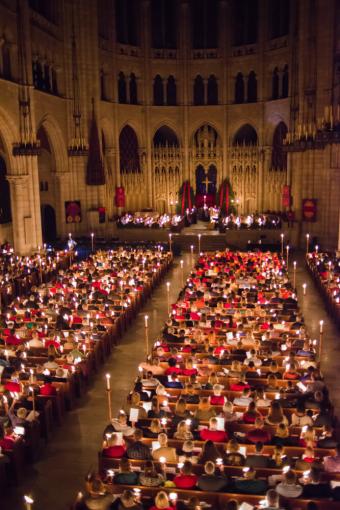 The interior of a church, its pews packed with people lit by the glow of candelight.