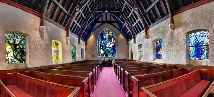 A wide angle lens photo of the inside of a church featuring many stained glass windows.