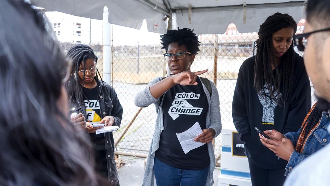 A woman in a Color of Change t-shirt offers directions to volunteers at an outdoor event