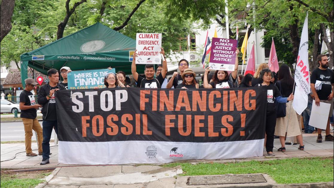 Donzens of people gathered behind a sign that reads Stop Financing Fossil Fuels