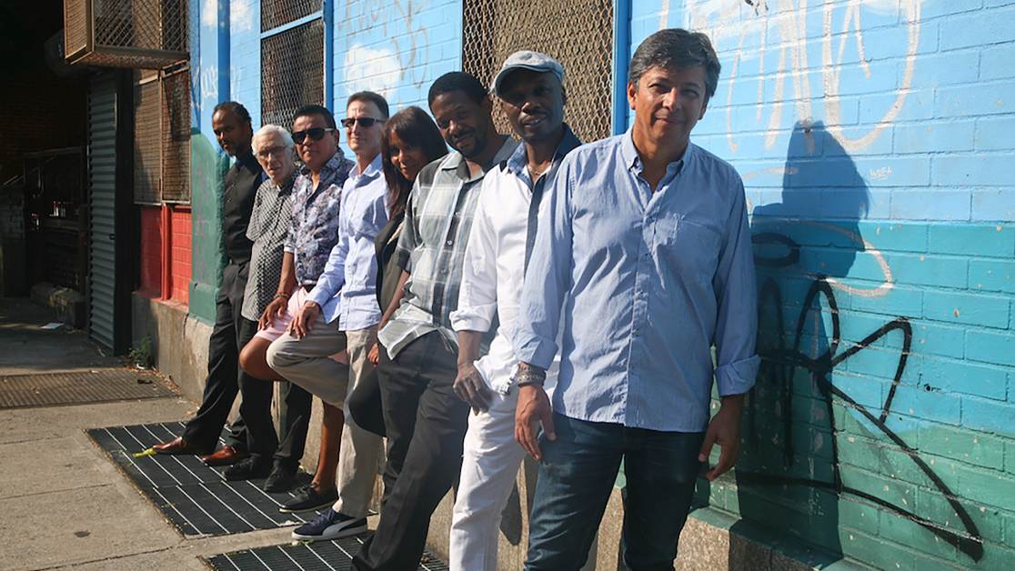 Men and women stand against a wall of graffiti