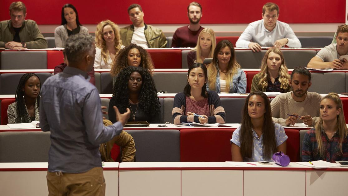Back view of man presenting to students at a lecture theatre