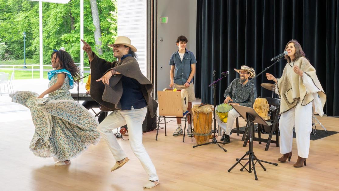 Performers dancing on stage, with instrumentalists accompanying them in the background.