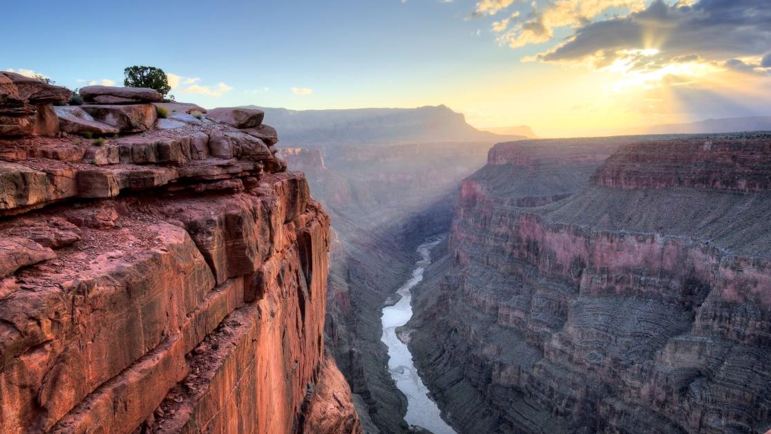 Two cliffs fall just shy of meeting as the sun rises over the Grand Canyon.