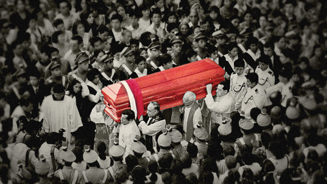 Clergy members carry a coffin through an enormous crowd of onlookers. The photo is black and white, except for the coffin, which is bright red. 