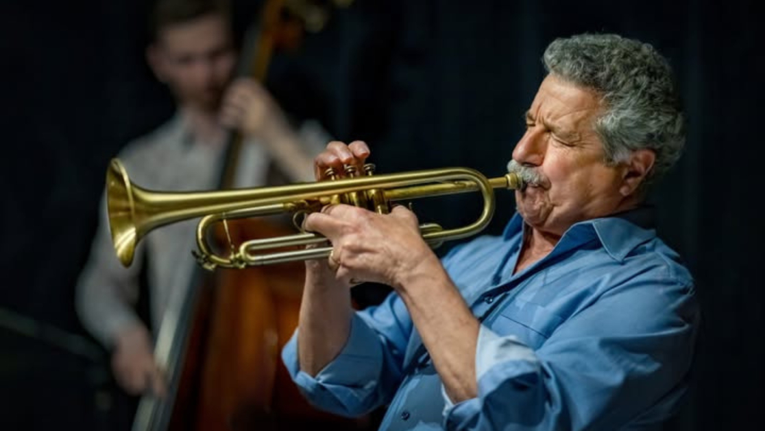 A man in a blue shirt plays a trumpet.
