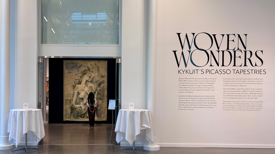 Visitor stands before a large Picasso tapestry at the entrance to the exhibition Woven Wonders: Kykuit's Picasso Tapestries, displayed in a bright gallery space.