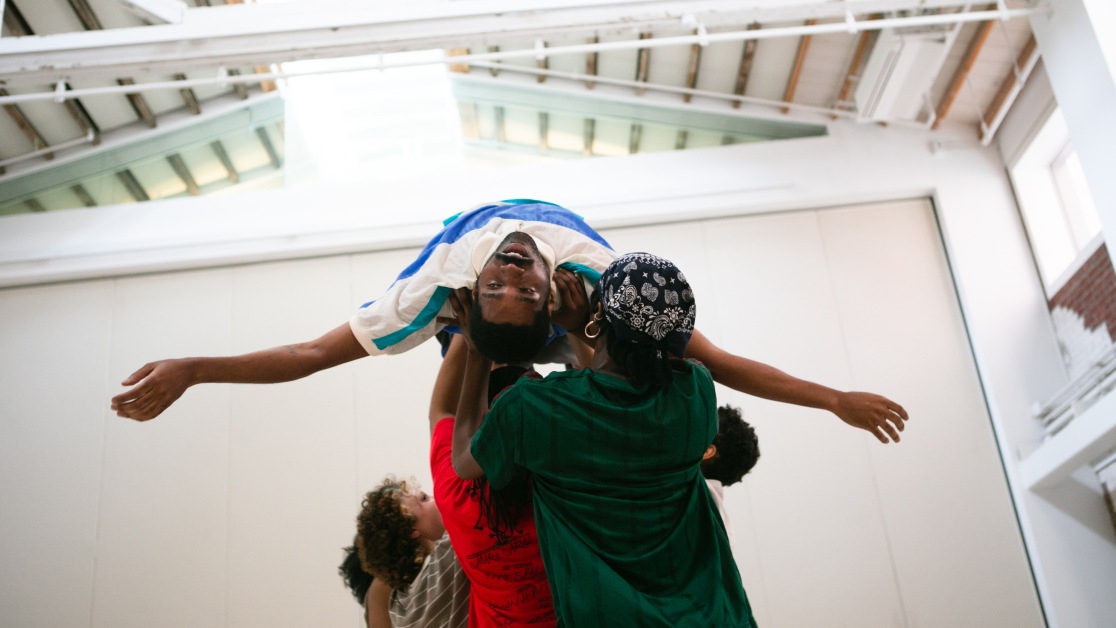 Dancers perform a lift in Kayla Farrish's A Beast That Came Apart Mid-Air. One performer is held horizontally overhead with arms outstretched while others support them from below,