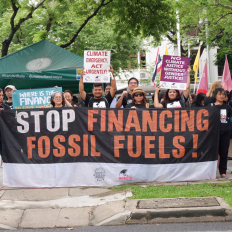 Donzens of people gathered behind a sign that reads Stop Financing Fossil Fuels