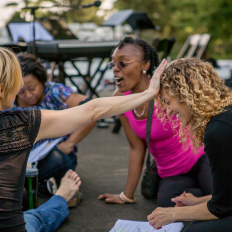 Four women laugh huddled over paperwork in an outdoor setting at Kykuit at Pocantico