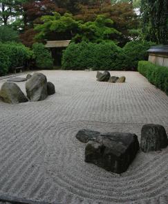 Rocks placed among patterned white gravel surrounded by green shrubbery