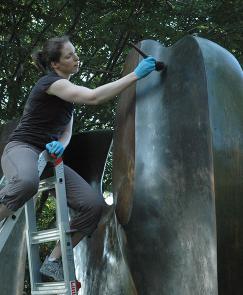 A woman on a ladder cleans a large outdoor sculpture