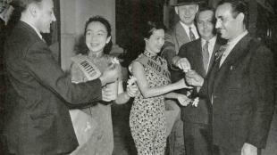 Two women wearing dresses stand in between several men wearing suits.