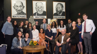 A large group of people poses in front of images of Gandhi, the Dalai Lama, and Martin Luther King, Jr.