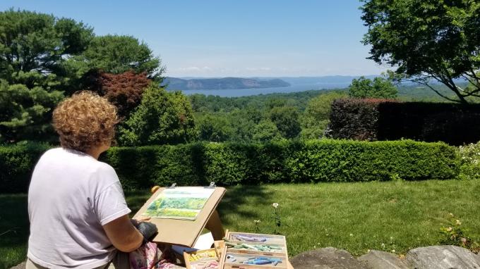 A woman paints the landscape of the Hudson valley in front of her.