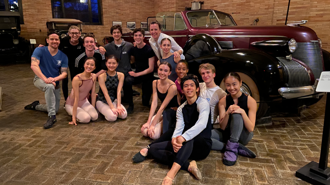 Ballet dancers pose in front of an antique car