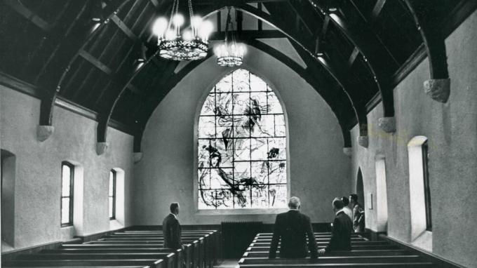 A black and white photo of the interior of a church featuring a large stained glass window.