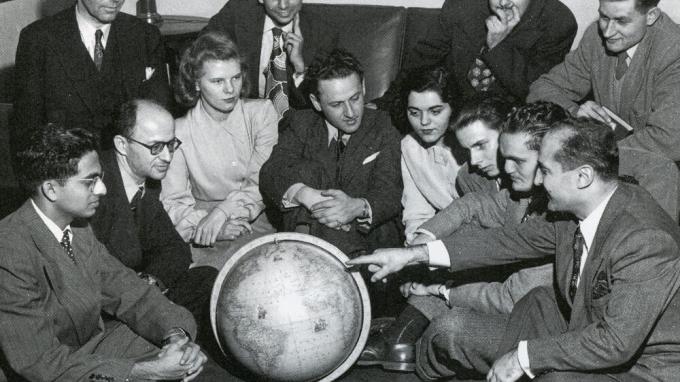 Black and white photo of a group of women and men gathering around a globe.