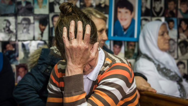 A woman with her head in her hands in front of a wall of photos