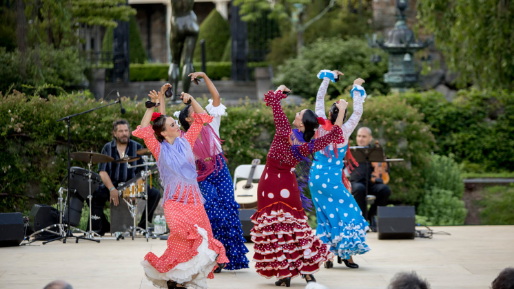 four female flamenco dancers in brightly colored, ruffled dresses perform on an al fresco stage